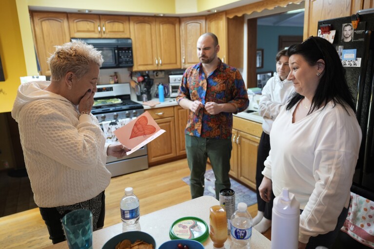 Deb Robertson, left, reacts to a card made for her by a student of her daughter Shannon Rodriguez, right, as her son Jake and niece Emma watch before a BBQ with family and friends at her Lombard, Ill., home Saturday, March 23, 2024. She didn’t cry when she learned two months ago that the cancerous tumors in her liver were spreading, portending a tormented death. But later, she cried after receiving a call that a bill moving through the Illinois Legislature to allow certain terminally ill patients to end their own lives with a doctor’s help had made progress. (AP Photo/Charles Rex Arbogast)